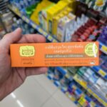 Sunbites Daily Nuts Daily Boost 5 in 1: Budget-Friendly Mixed Nuts with a Soft Texture Crunch A hand holding an orange box of Tepthai Concentrated Herbal Toothpaste Fresh Fruit with Fluoride inside a 7-Eleven in Thailand.