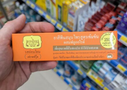 A hand holding an orange box of Tepthai Concentrated Herbal Toothpaste Fresh Fruit with Fluoride inside a 7-Eleven in Thailand.