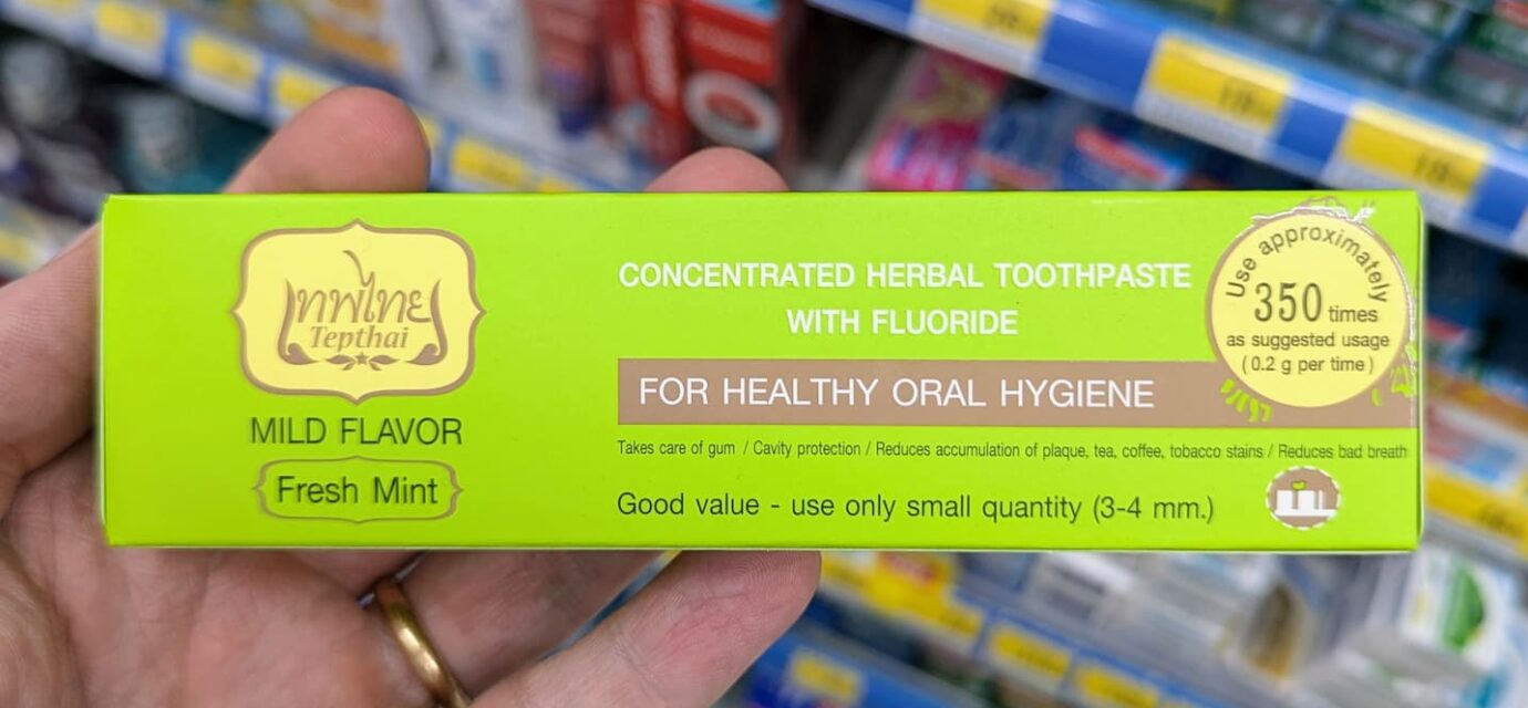 A hand holding a green box of Tepthai Concentrated Herbal Toothpaste Fresh Mint with Fluoride inside a 7-Eleven in Thailand.