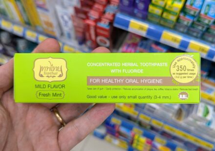 A hand holding a green box of Tepthai Concentrated Herbal Toothpaste Fresh Mint with Fluoride inside a 7-Eleven in Thailand.