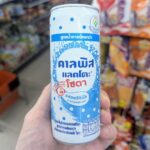 Ezygo Garlic Pork and Fried Egg with Rice: Quick Convenience Spoiled by an Unnatural Fried Egg A hand holding a slim white and blue polka-dot can of Calpis Lacto Soda Original Low Sugar inside a 7-Eleven store in Thailand.