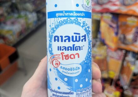 A hand holding a slim white and blue polka-dot can of Calpis Lacto Soda Original Low Sugar inside a 7-Eleven store in Thailand.