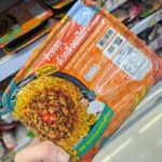 Ezygo Garlic Pork and Fried Egg with Rice: Quick Convenience Spoiled by an Unnatural Fried Egg A hand holding an orange tray of Chef Cares Rice Mixed with Yellow Curry Paste and Chicken Breast inside a 7-Eleven store in Thailand.