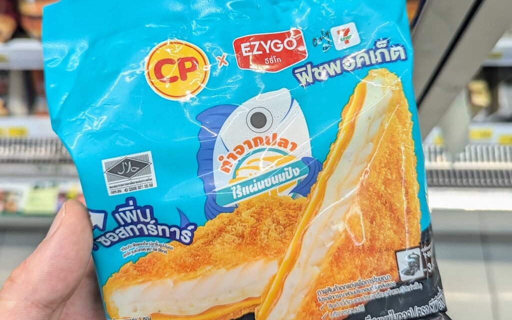 A hand holding a cyan-blue package of CP x Ezygo Fish Pocket inside a 7-Eleven store in Thailand.