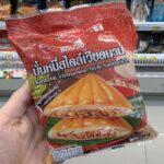 Calpis Lacto Soda Original (Low Sugar): Sweet, Bubbly Japanese Cultured Milk Refreshment A hand holding a red package of Ezygo Banh Mi Vietnamese-Style Sandwich in front of a 7-Eleven display in Thailand.