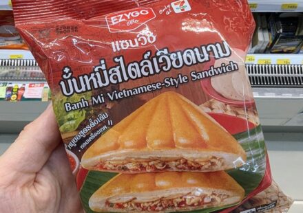 Ezygo Banh Mi Vietnamese-Style Sandwich: A Crunchy Asian Fusion Toastie That Hits the Spot A hand holding a red package of Ezygo Banh Mi Vietnamese-Style Sandwich in front of a 7-Eleven display in Thailand.