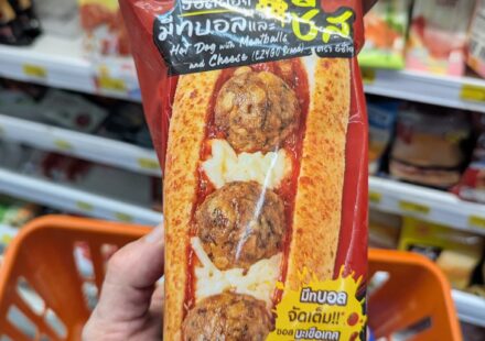 Ezygo Hot Dog with Meatballs and Cheese: A Satisfying Italian-Style Microwave Bit A hand holding a red package of Ezygo Hot Dog with Meatballs and Cheese inside a 7-Eleven store in Thailand.