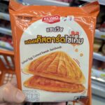 7-Eleven Thailand vs. 7-Eleven Japan: Which Country Has the Ultimate Convenience Store? A hand holding an orange package of Ezygo Salted Egg Custard Danish Sandwich inside a 7-Eleven store in Thailand.