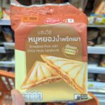 Ezygo Egg Salad Sandwich: Moist, Creamy, and Unbeatable Value for Anytime Snacking A hand holding a brown and beige package of Ezygo Shredded Pork with Chilli Paste Sandwich inside a 7-Eleven in Thailand.