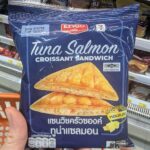 Ezygo Ham Cheese Croissant Sandwich: A Reliable 7-Eleven Classic That Never Fails A hand holding a navy-blue package of Ezygo Tuna Salmon Croissant Sandwich in front of a 7-Eleven display in Thailand.