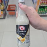 Ezygo Ham Cheese Croissant Sandwich: A Reliable 7-Eleven Classic That Never Fails A hand holding a 300ml glass bottle of Vitamilk Double Black Sesame and Black Rice soy milk inside a 7-Eleven in Thailand.
