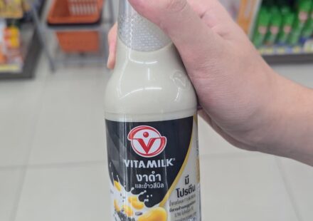 Vitamilk Double Black Sesame & Black Rice: Nutrient-Dense Plant Milk with a Satisfying Roasted Flavor A hand holding a 300ml glass bottle of Vitamilk Double Black Sesame and Black Rice soy milk inside a 7-Eleven in Thailand.