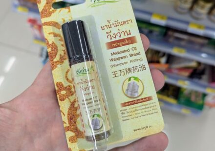 A hand holding a blister package of Wangwan Brand Medicated Oil Roll-On inside a 7-Eleven store in Thailand.