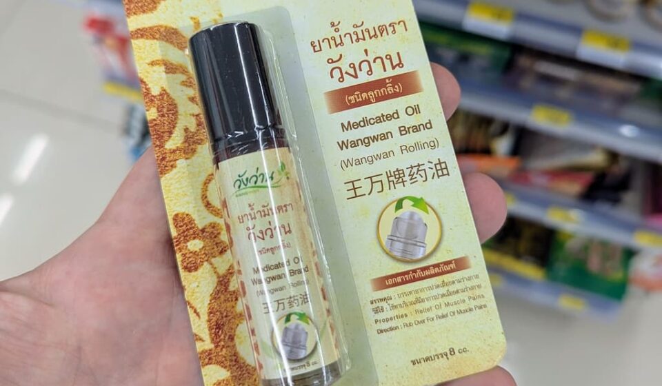 A hand holding a blister package of Wangwan Brand Medicated Oil Roll-On inside a 7-Eleven store in Thailand.