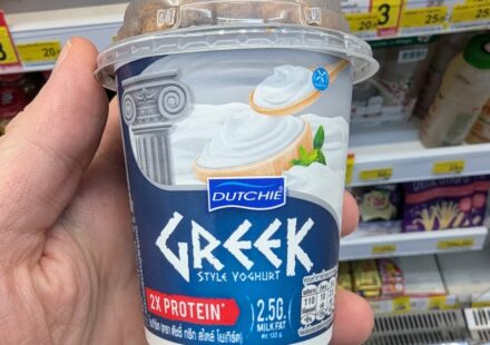 Dutchie Greek Style Yoghurt: Thick, Creamy, and High-Protein Value in Thailand A hand holding a blue cup of Dutchie Greek Style Yoghurt with granola dome inside a 7-Eleven store in Thailand.