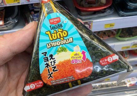 Ezygo Ebiko Mayonnaise Onigiri: A Crisp, Creamy Rice Snack That Hits the Spot Fresh A hand holding a triangular package of Ezygo Ebiko Mayonnaise Onigiri inside a 7-Eleven store in Thailand.