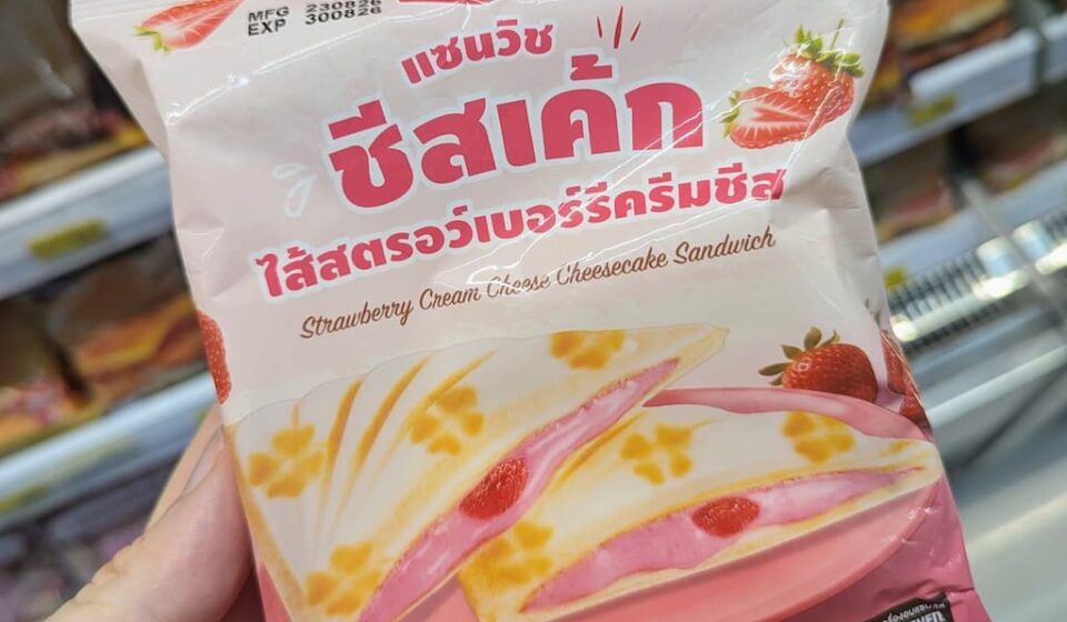 Ezygo Strawberry Cream Cheese Cheesecake Sandwich: A Sweet Dessert Toastie That Overpowers the Palate A hand holding a pastel pink package of Ezygo Strawberry Cream Cheese Cheesecake Sandwich inside a 7-Eleven store in Thailand.