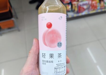 HEYTEA Peach Cranberry Green Tea: A Refreshing Chinese Fruit Tea Picked on Recommendation A hand holding a slim 450ml bottle of HEYTEA Peach Cranberry Green Tea inside a 7-Eleven store in Thailand.