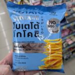 A hand holding a light blue bag of Koikeya Potato Kochi Original Flavor chips inside a 7-Eleven store in Thailand.
