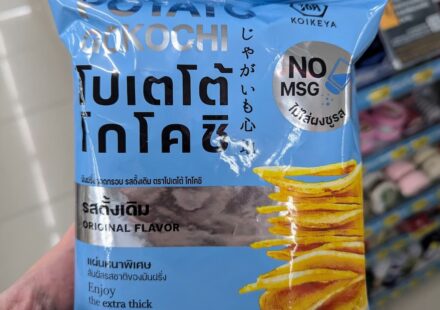 Koikeya Potato Kochi Original Flavor: Thick-Cut, Pure Potato Crunch with Zero MSG A hand holding a light blue bag of Koikeya Potato Kochi Original Flavor chips inside a 7-Eleven store in Thailand.