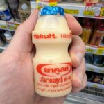 Ezygo Strawberry Cream Cheese Cheesecake Sandwich: A Sweet Dessert Toastie That Overpowers the Palate A hand holding an iconic 80ml bottle of Yakult Probiotic Cultured Milk in front of a 7-Eleven dairy display in Thailand.
